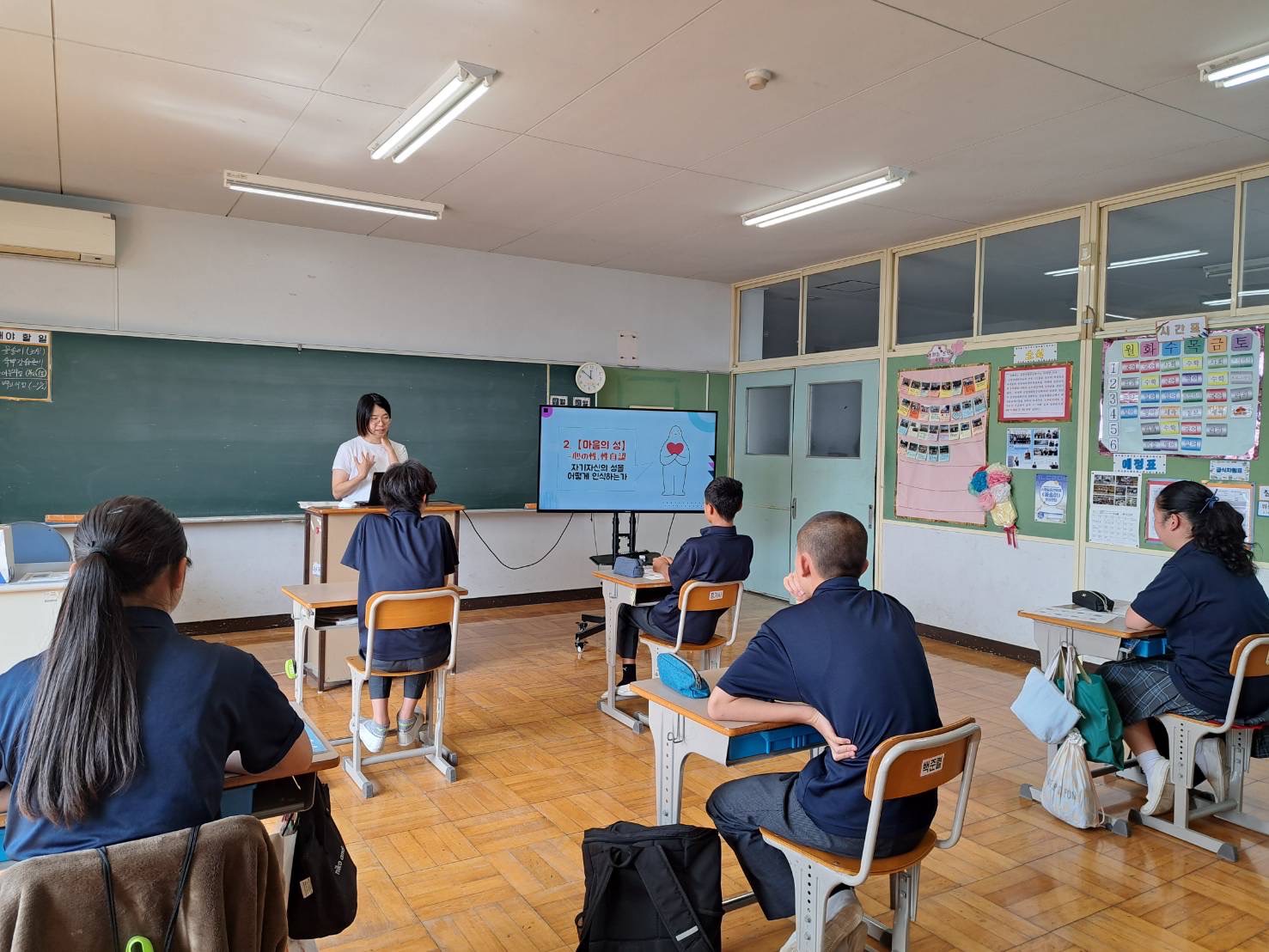 千葉朝鮮初中級学校の中２と中３への授業の様子。前方に講師と授業の教材を投影したモニター、後方に授業に参加する５人の生徒が写っている。